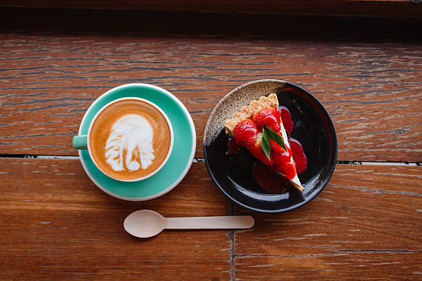 Top view of a cappuccino and a fresh strawberry tart on a dark wood table.