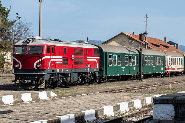 Bansko, Bulgaria - Mar 14, 2025: A classic red and green passenger train with a diesel locomotive waits on tracks at an old train station