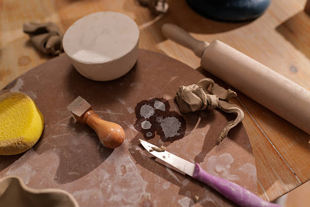 Arranging various pottery tools alongside a lump of clay on a wooden table in a pottery workshop, highlighting the essential elements of the craft and the artist's creativity