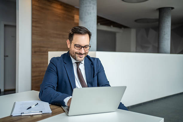 istock Smiling businessman in suit working on laptop 2252832525