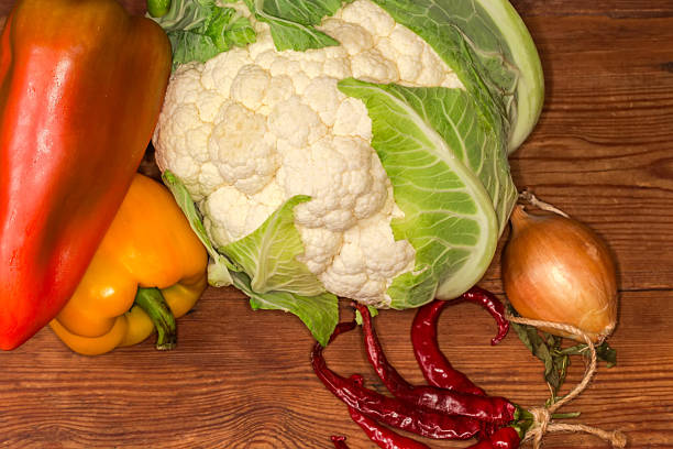 Whole raw head of the freshly harvested cauliflower among the other fresh vegetables on an old wooden rustic table, fragment close-up
