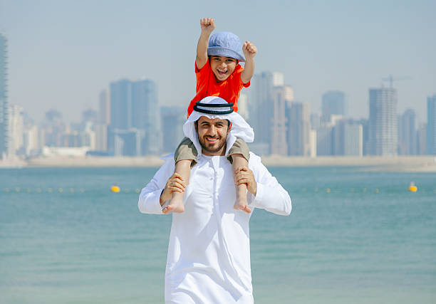 istock Smiling Arab Father Carrying Young Son on His Shoulders While Playing at the Beach with Dubai Skyline in the Background 2252835885