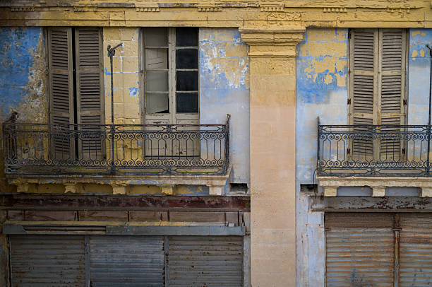 Weathered facade of an old building. The peeling paint and rusted shutters show the passage of time and the building's slow decay.