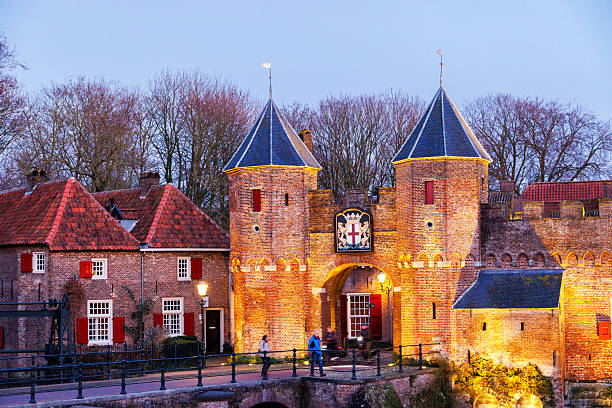 Amersfoort, The Netherlands. December 19th, 2025: A serene nighttime view of the Koppelpoort, a historic medieval city gate and bridge. Illuminated by warm streetlights, its reflection shimmers beautifully in the calm water of the canal. The scene captures the enchanting atmosphere of Amersfoort's historic charm.