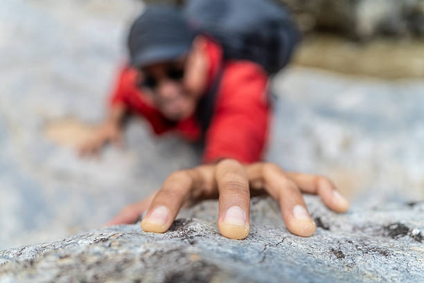 Handsome asian hiker climber carefully grips a rock while scaling a steep cliff during a hike in a national park.