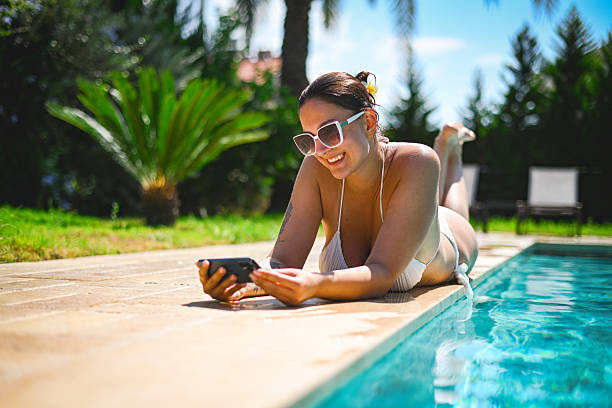 A woman relaxing by the pool and enjoying her vacation, using a mobile phone