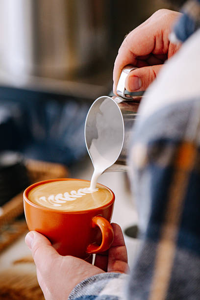Close-up of barista hands pouring steamed milk into coffee cup to create latte art in a cafe