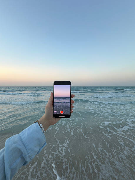 istock Woman's hand holding smartphone recording ocean waves at sunset 2252841495