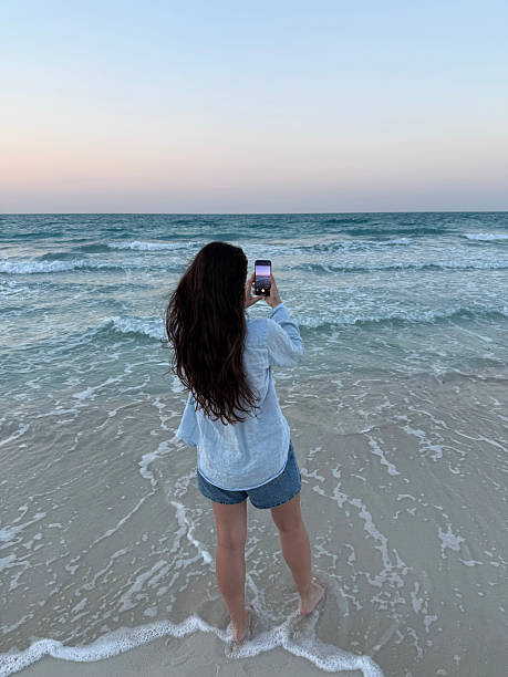 istock Woman capturing ocean sunset with smartphone while standing on beach 2252842247