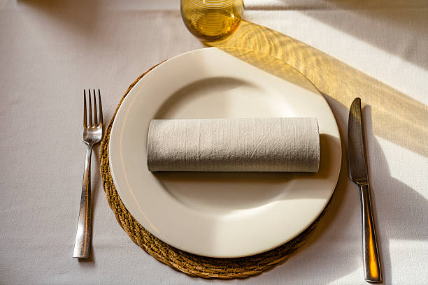 Elegant and minimalist place setting shot from above on restaurant table. Textile tablecloth and napkin, fork and table knife and drinking glass.