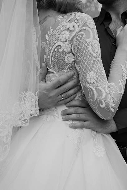 Black and white photo of a bride and groom holding hands during a wedding ceremony, showcasing intimacy and elegance.