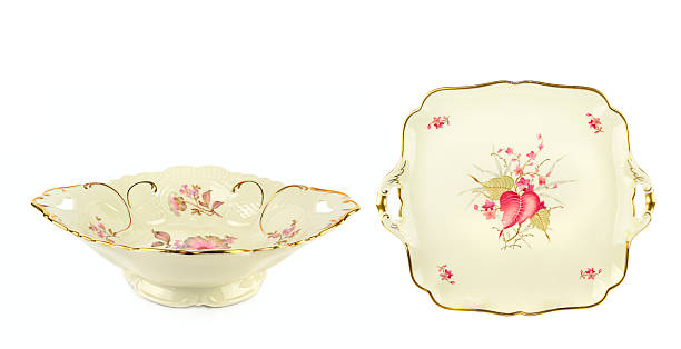 An elegant ivory porcelain bowl and matching tray decorated with pink floral patterns and gold rims. This isolated studio shot with copy space is ideal for vintage decor and antique themes.