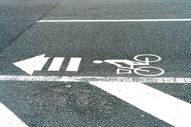 White painted bicycle icon and directional arrow on dark asphalt road surface. Clear marking for dedicated cycling path and urban traffic management. High angle view of pavement texture.