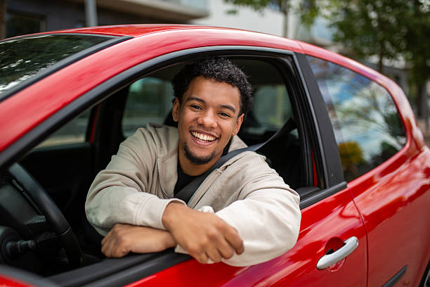 Young man leaning out of the driver’s seat window of a red car, smiling cheerfully