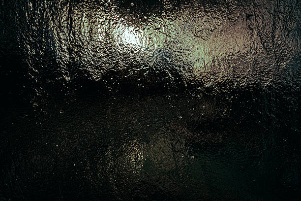 close-up dynamic texture of dark water flowing down a transparent surface glass panel. Use as a background, texture overlay, tranquility, moody, dullness, boredom