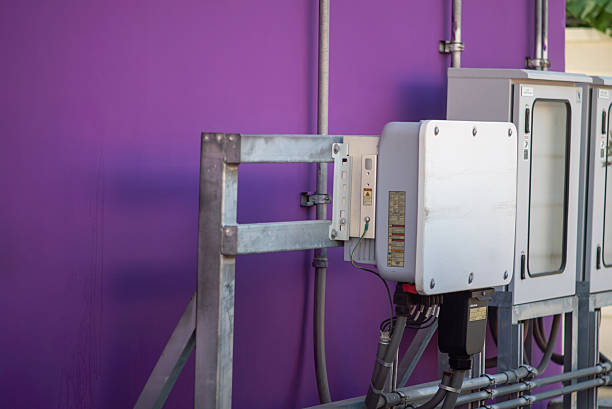 A close-up view of modern electrical equipment mounted on a vibrant purple wall, showcasing cables and control panels in an urban setting.