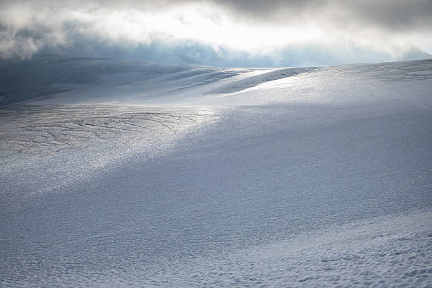Minimalist alpine glacier landscape covered with fresh snow and soft light breaking through low clouds. Abstract winter scene with smooth ice surface, gentle slopes and dramatic atmosphere, symbolizing isolation, purity, climate and untouched nature