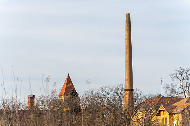 Tall industrial chimney dominating the skyline of a historic complex. The contrast between vertical structure and open sky creates a strong architectural composition.