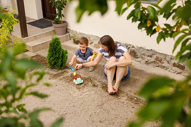 High angle view of mother and toddler son having fun playing in sand, digging holes and transporting sand in a toy truck
