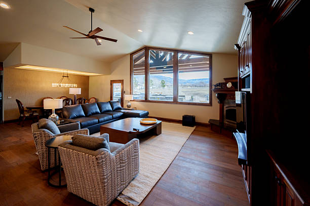 Luxury home interior featuring a spacious living room with modern furnishings, hardwood floors, fireplace, and large windows providing natural daylight. Open layout and refined finishes present an upscale residential interior designed for comfort and functionality.