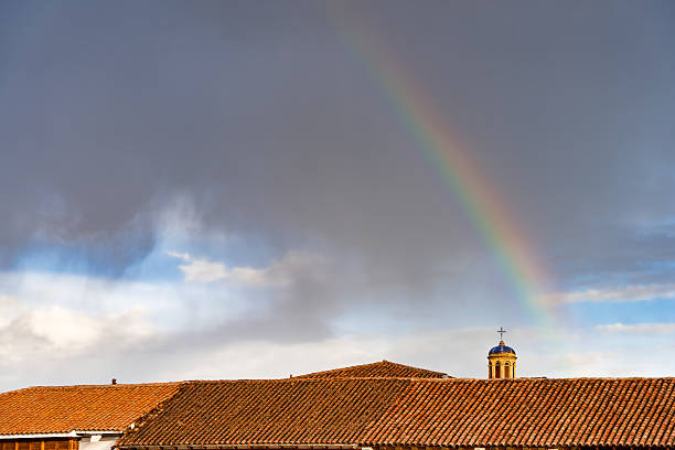 A vibrant rainbow over traditional colonial style buildings in Paza de Armas, Cusco and a church dome in the background.