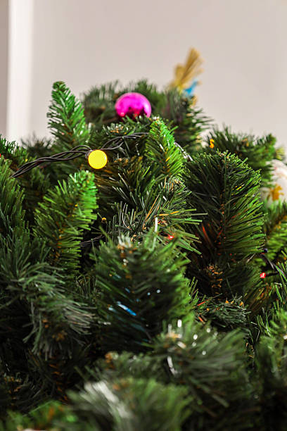 istock Close-up of fluffy artificial Christmas tree branches decorated with a vibrant pink bauble and twinkling yellow garland lights. 2252878004