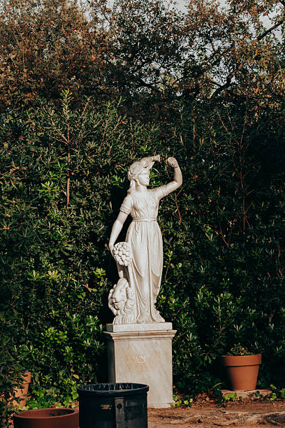 Classical stone statue of a female figure surrounded by dense vegetation in a historic garden in Sant Gervasi, Barcelona. Outdoor cultural heritage scene with autumn colors.