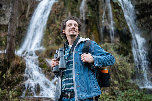istock Adventurous Traveler With Binoculars By A Waterfall In A Lush Forest 2252890892