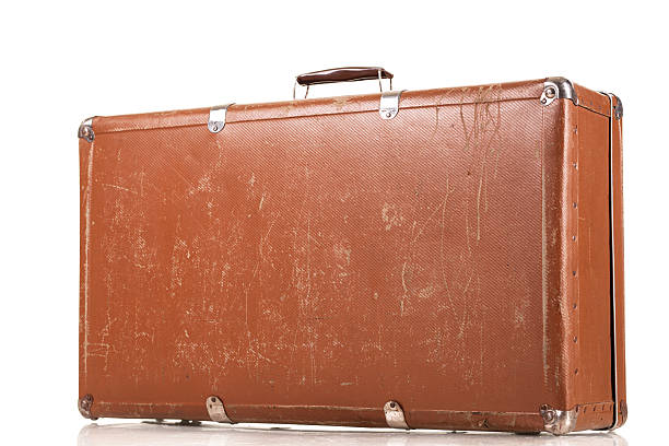 The brown vintage suitcase sits alone on a white surface, showcasing its worn texture and small scratches. Its handle and overall appearance suggest a long history of travel