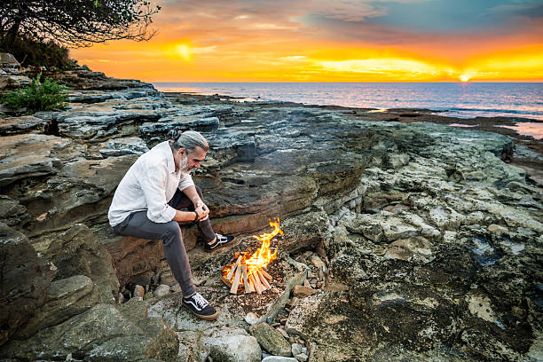 istock Man Sitting by Campfire on Rocky Terrain at Sunset 2252899231