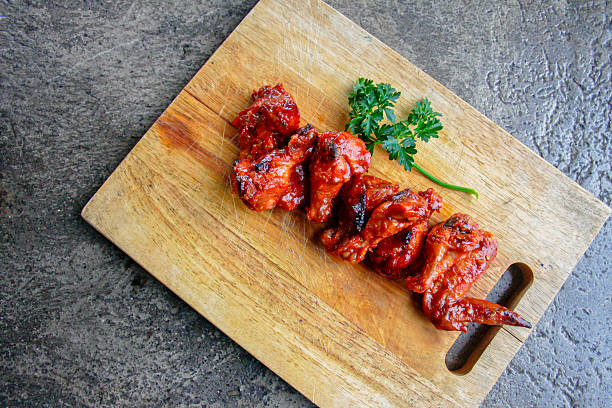 Overhead view of spicy glazed chicken wings arranged neatly on rustic wooden board. Concept image for restaurant menus, barbecue meals, spicy cuisine, and food banner design