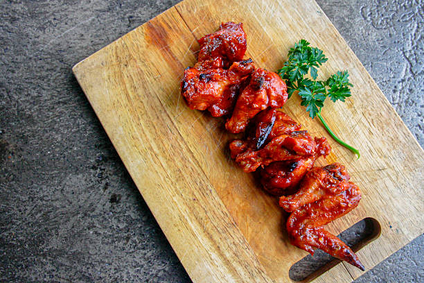 High-quality overhead image of spicy chicken wings coated in hot sauce on rustic wooden board with copy space. Concept for bar food, BBQ menus, food marketing and advertising