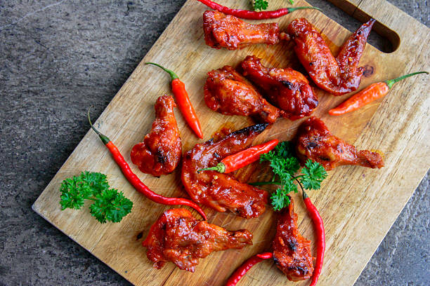 Overhead view of spicy glazed chicken wings with red chili peppers on rustic wood. Concept for hot food, comfort cuisine, street food, barbecue meals, and casual dining visuals