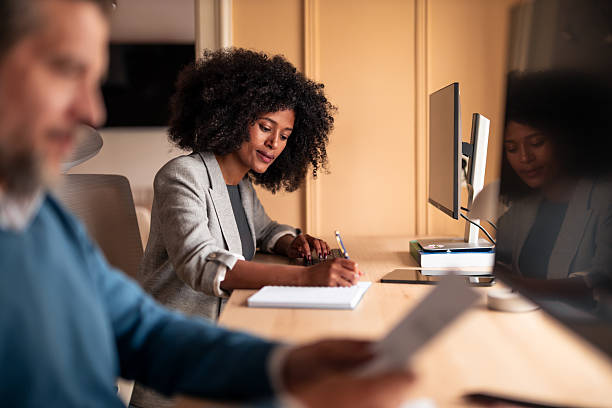 istock Professional Woman Writes Notes At Shared Desk While Colleagues Work Nearby In Modern Office 2252901558
