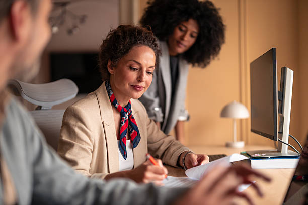 istock Business Meeting: Woman Writing Documents at Desk While Colleague Watches in Modern Office 2252901666