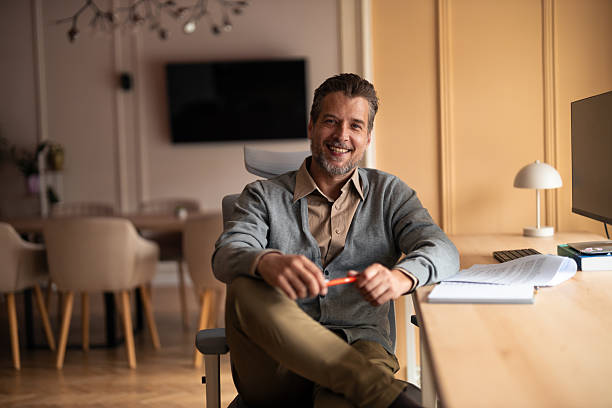 istock Smiling Man At Home Office Desk With Papers And Pen In Warm Light 2252901712