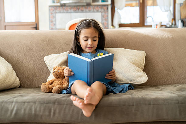 istock A young girl reading a book on the couch 2252903145