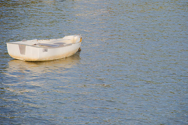 A lone white rowboat rests on a tranquil body of water, its reflection shimmering in soft light. The scene conveys solitude, calm, and simplicity, ideal for themes of leisure, travel, and nature.