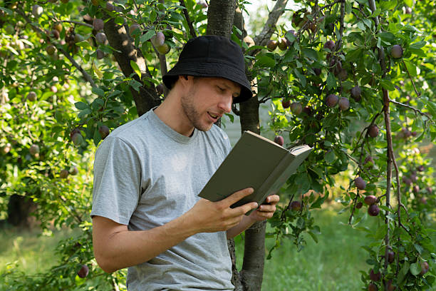 Cropped shot of peaceful young man holding cup of coffee and reading book on couch at home.