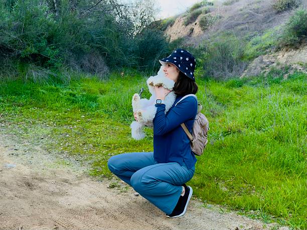 On the weekend a female person is hiking near Weir Canyon Nature Preserve with a little female dog  (domestic animal) Maltipoo beige color. Enjoying time with puppy picking up and holding her in the hands near face and embracing her. Outside is a nice warm weather. December 2025.