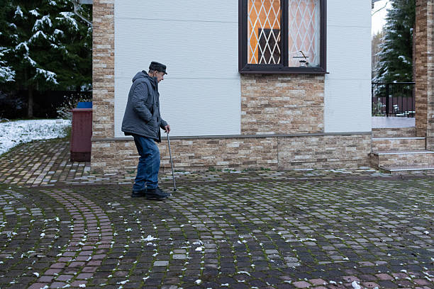 istock Elderly man walking with cane on snowy paved yard in winter 2252923093
