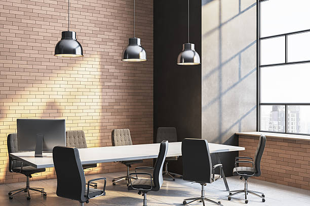 istock Modern corporate meeting room with sunlight casting shadows through large windows onto brick and concrete walls in an empty workspace setting. 3D Rendering 2252925921