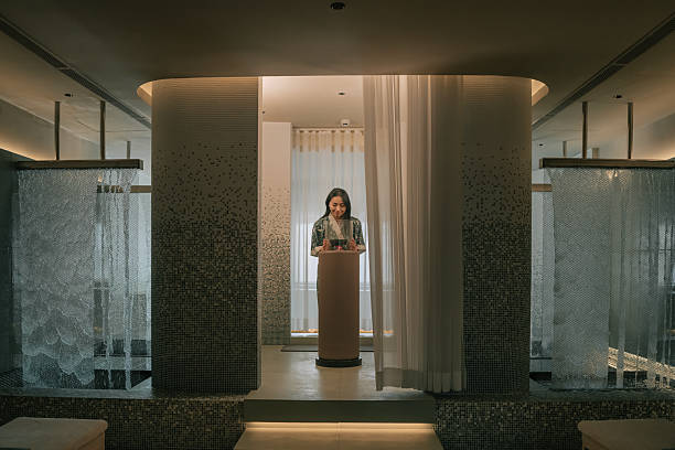 Asian female in a robe smells an essential oil diffuser as part of a pre-soak ritual before entering a luxury spa thermal pool area with steam and warm water, conveying relaxation, wellness, and self-care. Kuala Lumpur