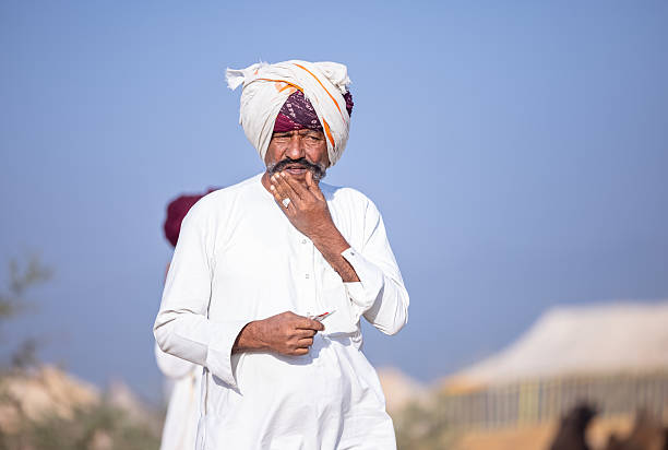 Pushkar, Rajasthan, India - November 2024: Portrait of a rajasthani male in traditional white clothes with colourful turban at desert fair ground during the pushkar camel fair to trade camels.