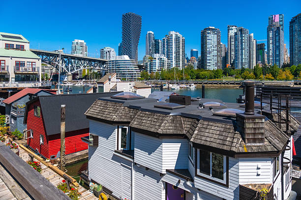 Colorful floating homes dotting false creek, framed by modern skyscrapers, create a vibrant urban scene in vancouver, british columbia, canada, under a sunny blue sky