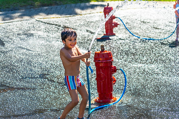 Smiling child is playing and splashing with water jets coming out of a fire hydrant in a public park in vancouver, british columbia, during a hot summer day