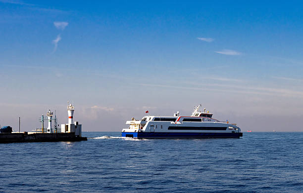 istock Passenger ferry exits harbor past striped lighthouse—captured in maritime transport composition with calm water, navigational structures, and clear daylight atmosphere. 2252932543