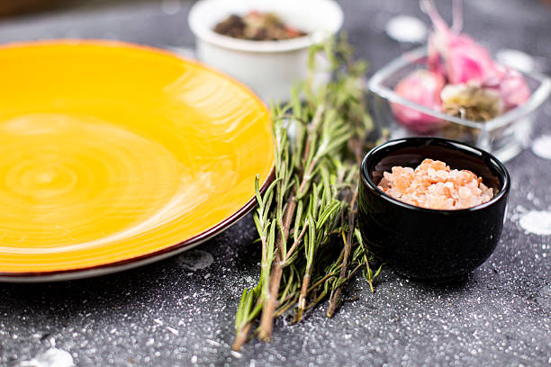 Ingredients are set on a kitchen counter. There is an empty yellow plate, fresh herbs, spices, and a small bowl of finely chopped shrimp ready for cooking.