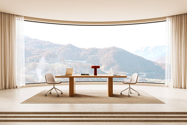 Contemporary office interior design featuring a wooden desk, swivel chairs, and a panoramic mountain view through a curved glass wall. 3D Rendering