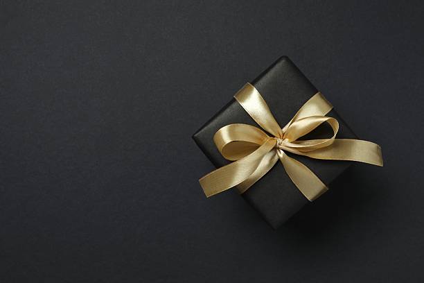 istock Beautiful gift box tied with golden bow on black background 2252945346